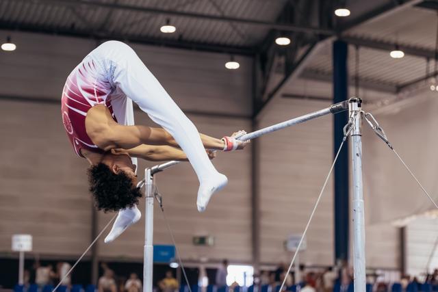 Young gymnast performs a dramatic arch on the uneven bars, body inverted, legs extended, in an indoor sports hall.