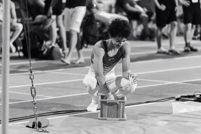 Young gymnast crouches intently over a chalk box on an indoor athletics track, preparing for a routine.