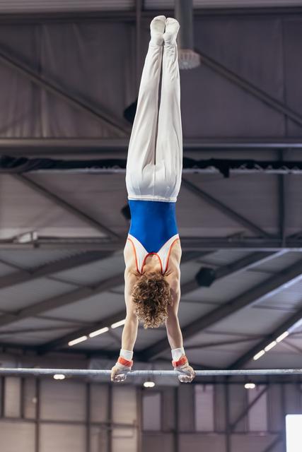 Young male gymnast performs a perfect handstand on horizontal bar, body fully extended, in indoor gymnasium.
