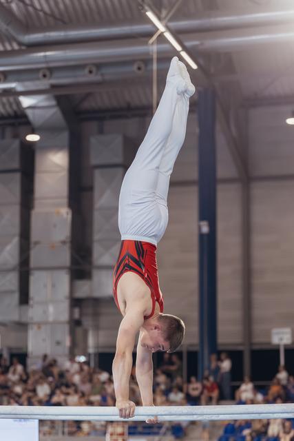 Young male gymnast performs a perfect handstand on parallel bars, legs split, intense concentration visible on his face.