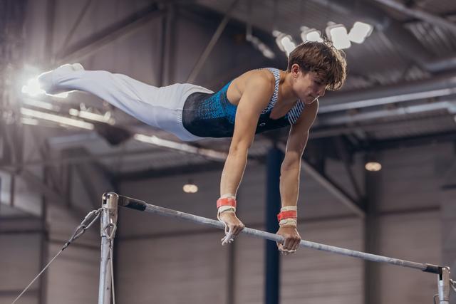 Young male gymnast performs a horizontal bar routine, body horizontal, intense focus, in an indoor sports hall.