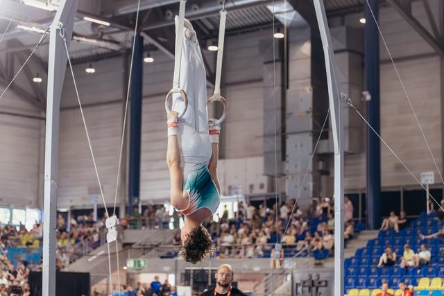 Gymnast performs an inverted hang on still rings, body straight and controlled, before a packed indoor arena audience.