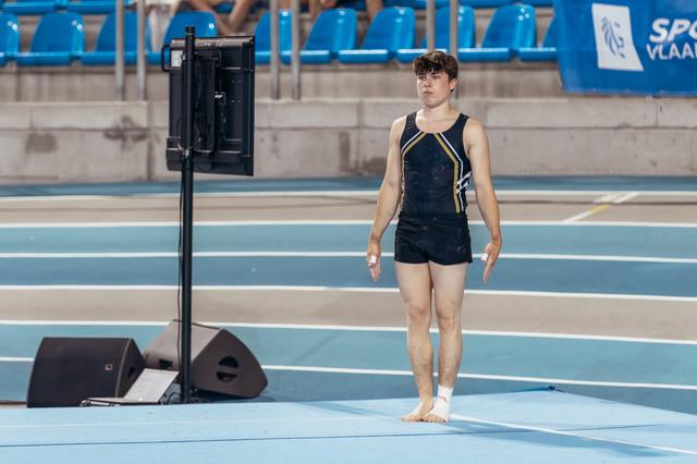 Young male gymnast stands barefoot on the floor exercise mat, composed and focused, preparing for his routine.
