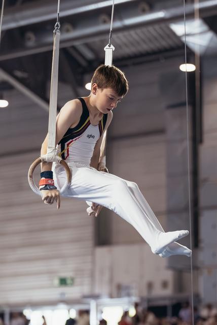 Focused young male gymnast holds a still rings position with intense concentration in a competition hall.