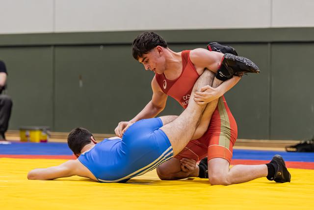 Geconcentreerde jongeling in rood pak tilt het been van zijn tegenstander op en domineert de blauwe sporter op de gele mat.