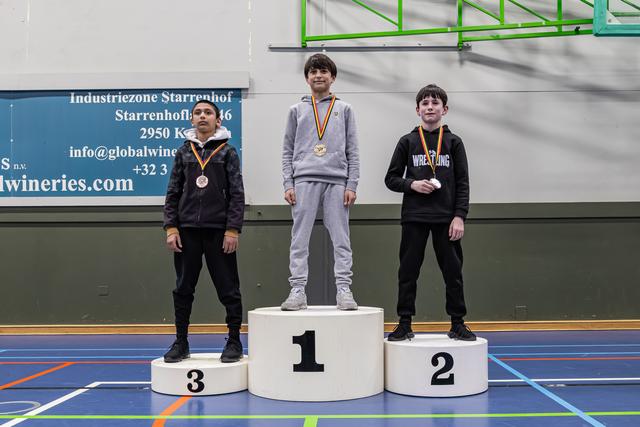 Drie jonge worstelaars op het podium; de gouden medaillewinnaar staat trots in het midden, geflankeerd door de brons- en zilverwinnaars.