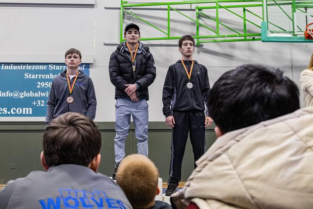 Drie tieners staan ernstig en beheerst op het podium met medailles om in een sporthal.