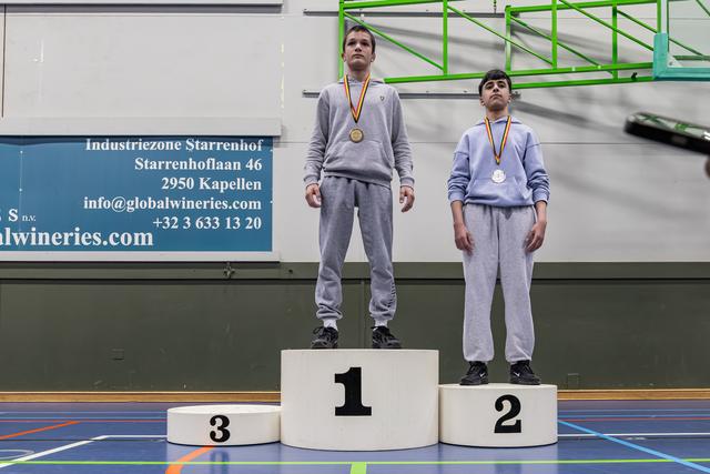 Twee jonge atleten staan op de eerste en tweede plaats van het podium, met medailles om, ernstig en beheerst van uitdrukking, in een sporthal.