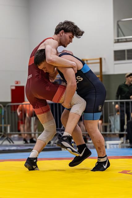 Twee jonge worstelaars verwikkeld in een fel duel op de gele mat, zichtbaar gespannen tijdens een indoortoernooi.