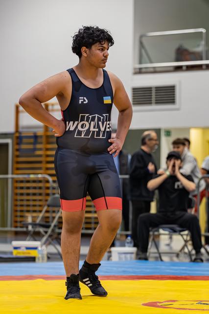 Jonge worstelaar in Wolves-tenue staat zelfverzekerd met handen in de zij en kijkt de zaal in tijdens een wedstrijd.
