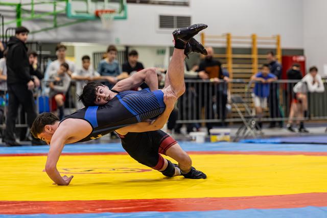 Jonge worstelaar in blauw pak voert een krachtige suplex uit en gooit zijn tegenstander in de lucht op de wedstrijdmat.