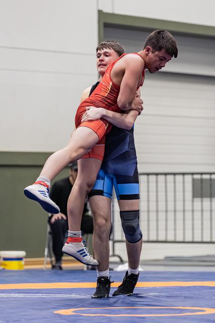 Jonge worstelaar in blauw tilt tegenstander in rood van de mat, met kracht en vastberadenheid tijdens een wedstrijd.