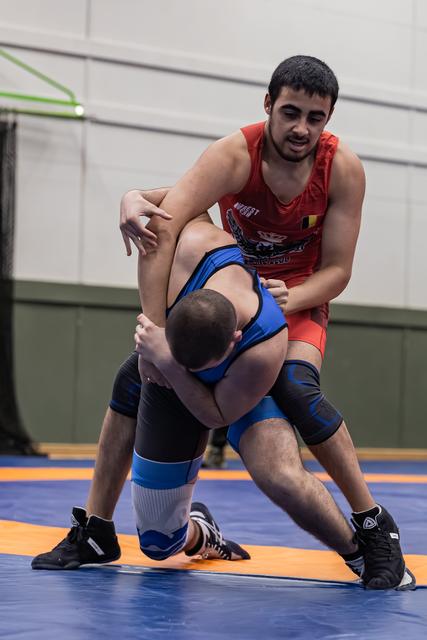 Jonge worstelaar in rood tenue overheerst tegenstander in blauw met stevige greep op de wedstrijdmat.