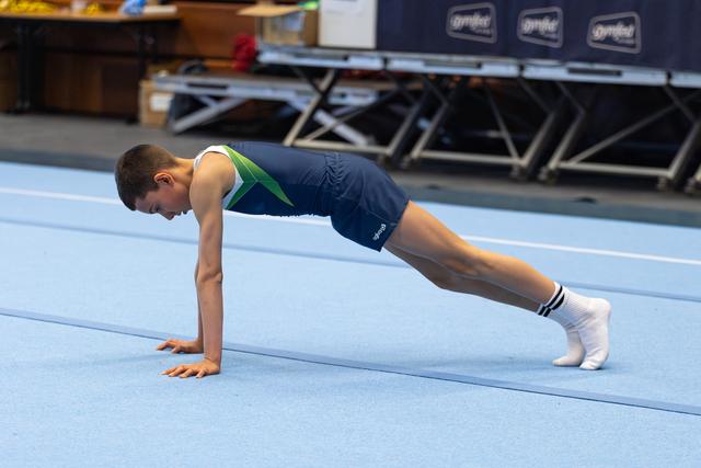 Young athlete holds a perfect plank position during floor exercise warm-up on spring floor at indoor training facility