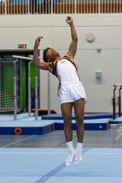 Young athlete jumps with raised fists in celebration, wearing white uniform with colored trim, in indoor sports facility