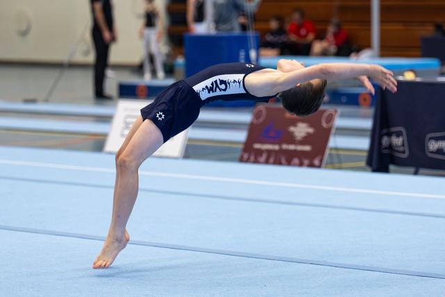 Young athlete performing a backward layout jump during floor routine, body fully extended and arched in mid-air