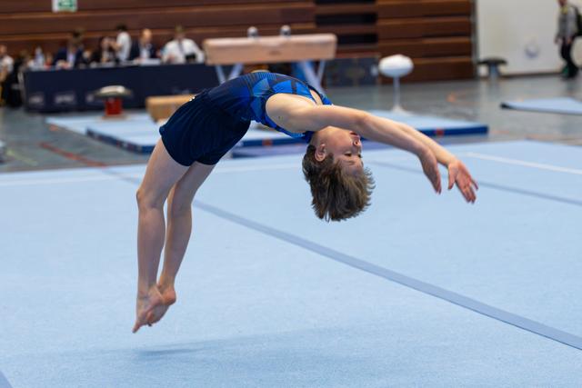 Young athlete executes a graceful backward arch mid-air during floor routine, arms extended with focused expression