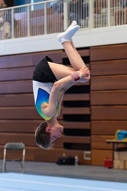 Young athlete executing a backflip mid-air with focused expression, wearing colorful leotard in indoor training facility