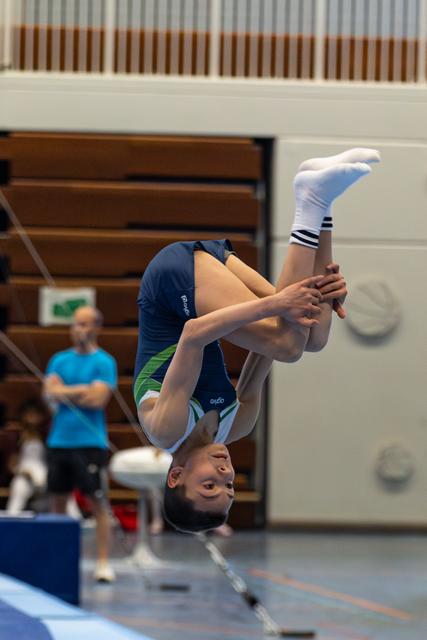 Young athlete executing a backflip in tucked position during floor exercise routine in indoor sports hall