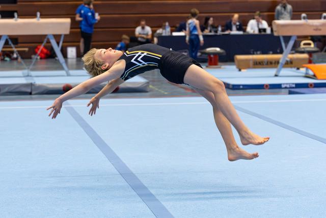 Young gymnast mid-air performing a powerful backflip during floor exercise routine in an indoor sports arena