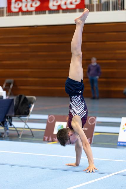 Gymnast executing a vertical handstand with straight body alignment during floor exercise routine in indoor sports hall
