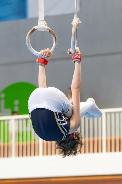 Young gymnast performing an inverted hang position on still rings during training, demonstrating strength and control