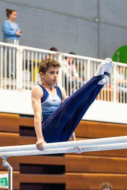 Young athlete performing an L-sit hold on parallel bars during training, displaying strength and focus in the gymnasium