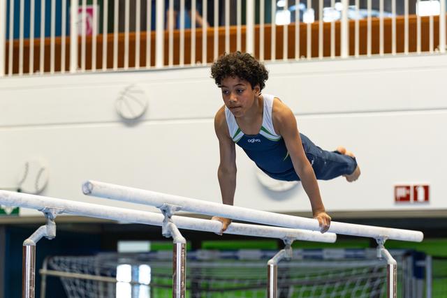 Young athlete performs a dynamic parallel bars routine, body horizontal in mid-air showing strength and control