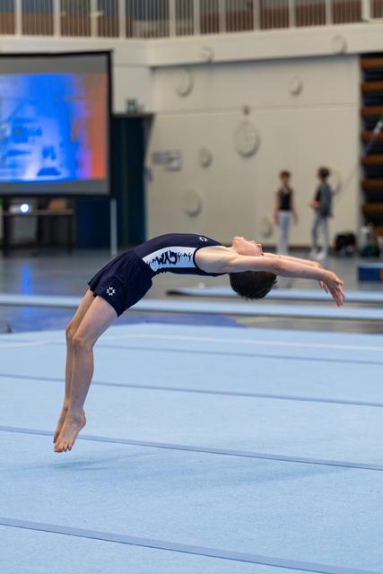 Young athlete executes a dramatic backward arch during floor exercise routine at indoor training facility