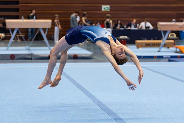 Athlete performing backward somersault mid-air during floor exercise routine at indoor championship event