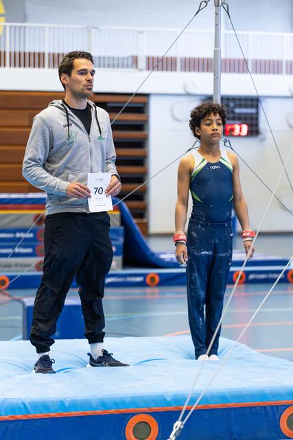 Coach and young athlete standing on floor mat awaiting performance score, focused expressions in training facility