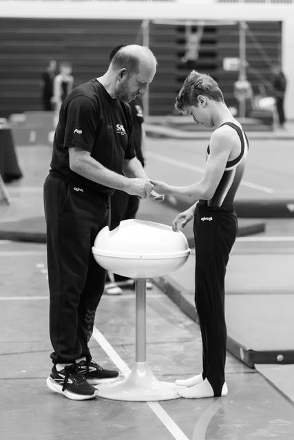 Coach carefully wraps protective tape around young athlete's wrist during training session in indoor sports facility