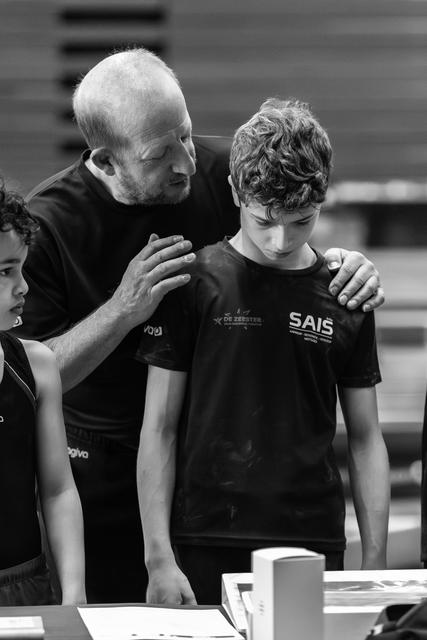 Coach with hand on shoulder of young athlete looking down, offering comfort and support during sporting event