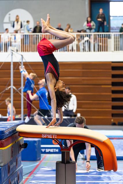 Female gymnast performs vertical handstand on vault with pointed toes during indoor training session