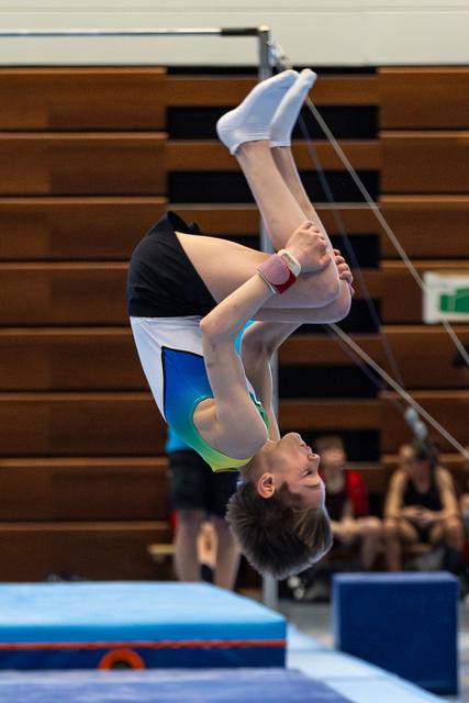 Female gymnast executes a tight back flip mid-air on trampoline, demonstrating focus and control during indoor training