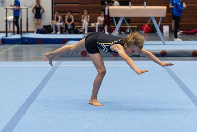 Female gymnast performing arabesque balance on floor mat, body extended horizontally with focused concentration during training