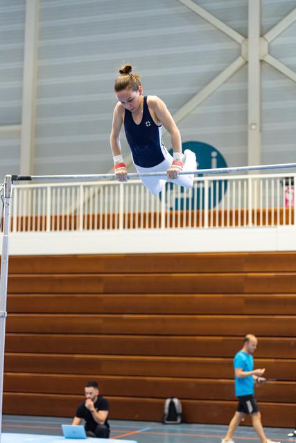 Female gymnast executes a handstand on uneven bars with focused concentration during indoor training session