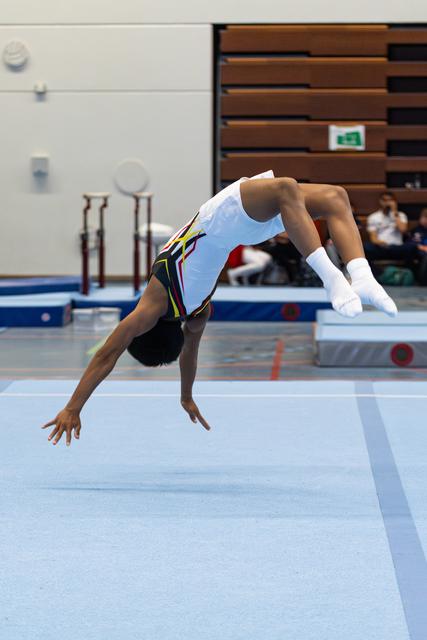Athlete performing a dramatic back walkover on floor exercise mat, arching deeply with head near ground in indoor facility