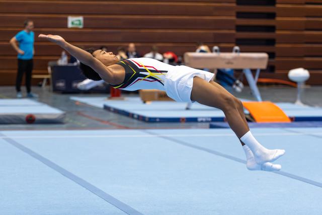 Athlete performs dynamic backbend leap on floor exercise mat during indoor training session