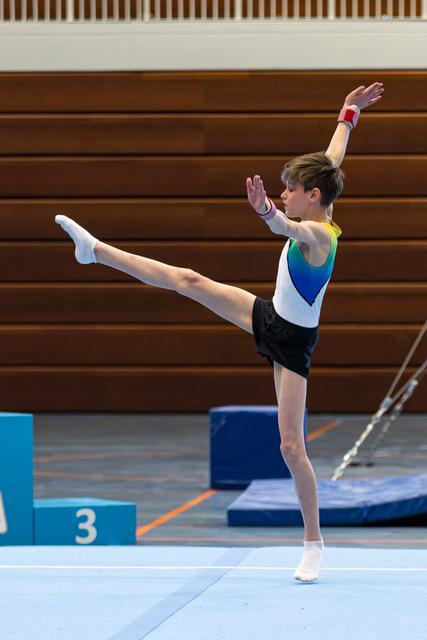 Athlete performs a front scale balance on floor, leg extended high, arms raised gracefully in colorful leotard