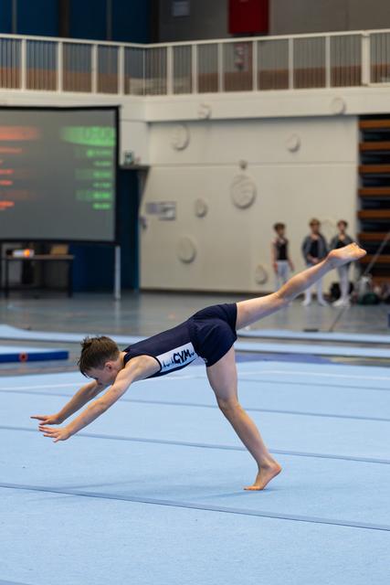 Athlete performs inverted pike position during floor routine, demonstrating strength and control on blue mat in indoor facility