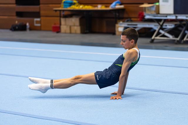 Young athlete demonstrates an L-sit position on floor mat during training, showing strength and control with pointed toes