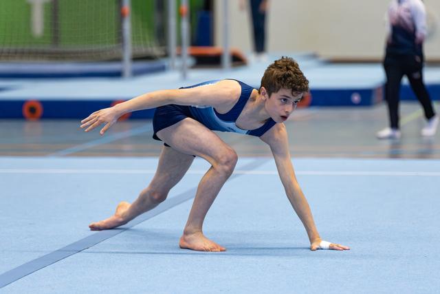Young athlete in navy leotard strikes a dramatic starting pose on floor mat, displaying intense focus and athletic form