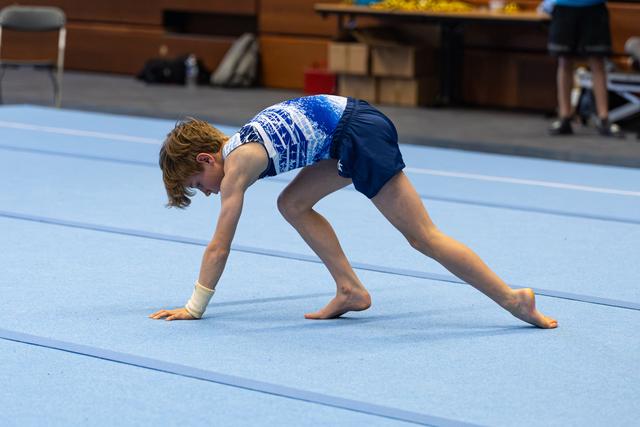Young athlete performs bridge position during floor routine, demonstrating flexibility and strength on blue spring floor