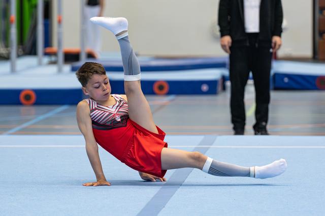 Athlete performs floor routine with leg raised vertically while seated, displaying strength and flexibility during performance