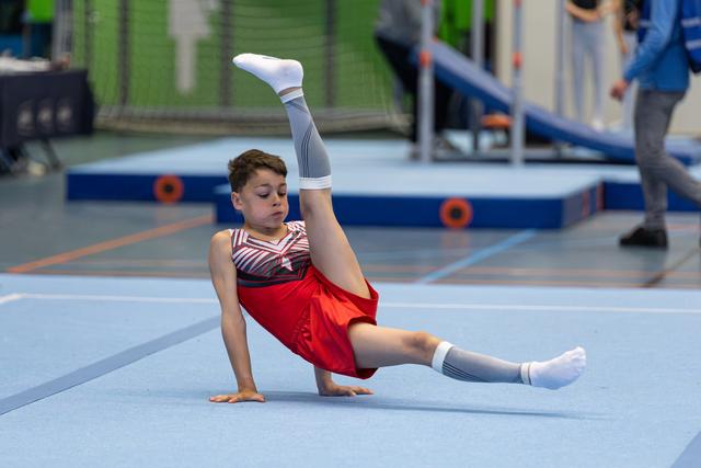 Young athlete performs floor routine with impressive split leg position, demonstrating flexibility and control on blue mat