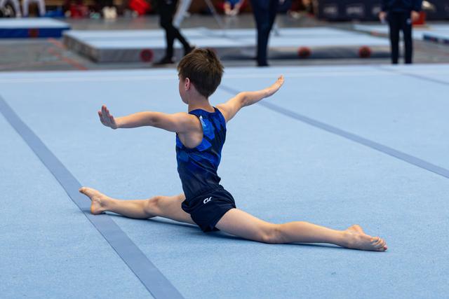 Young athlete performs floor split with arms extended during routine at indoor championship event