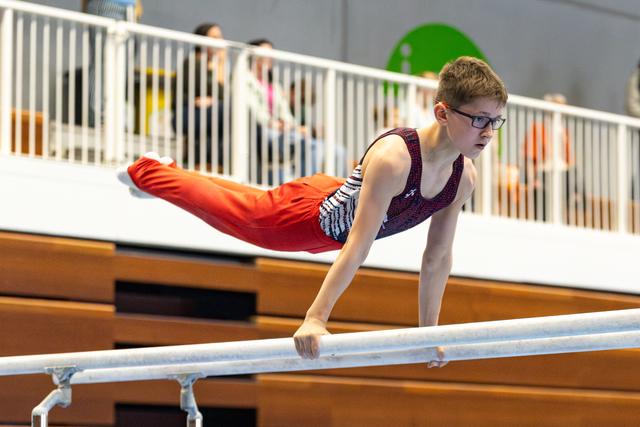 Young gymnast holds a horizontal position on parallel bars, demonstrating strength and concentration while wearing glasses