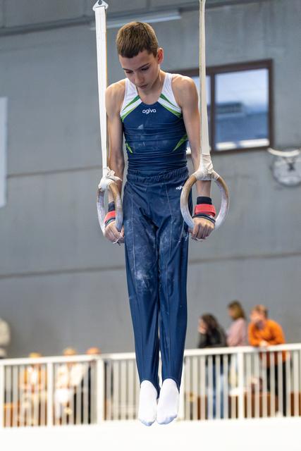 Young athlete performing a still rings routine, displaying intense concentration and control during competition