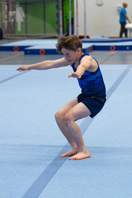 Young athlete in blue attire practicing landing technique with arms extended forward and knees bent on spring floor